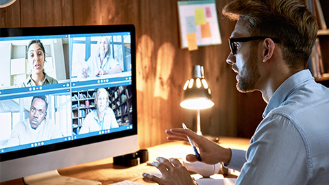 Businessman executive leading virtual team meeting on video conference call using computer working from home office talking to diverse colleagues in