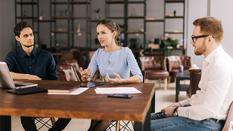 Confident young businessman presenting project to clients, making business offer, convincing customers to close deal in modern office meeting against large window.