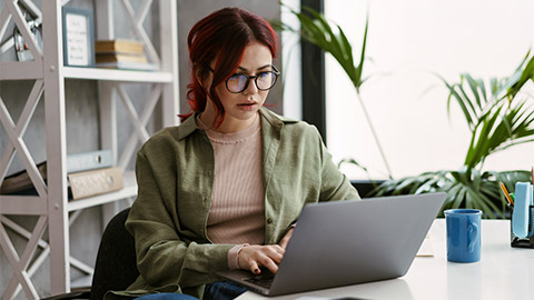 Young focused woman with red hair working with laptop while sitting in office