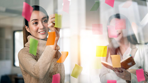 Colleagues writing on sticky notes on a glass window