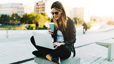 a person sitting alone on a stone bench with a laptop and a cup of coffee on one hand