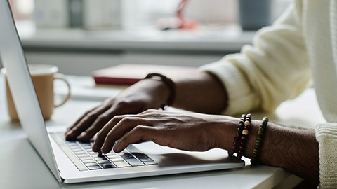 Hands of young unrecognizable businessman wearing white sweater pressing keys of laptop keyboard while working in the internet