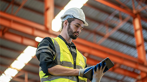 Low angle view of a worker wearing reflective jacket holding digital tablet standing in factory warehouse