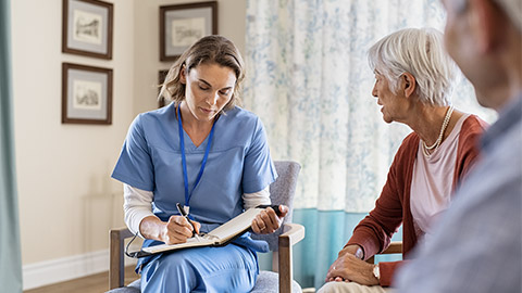 Young healthcare worker visiting senior couple at care centre and writing information.