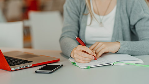 hands of female writting on notebook in cafe with laptop