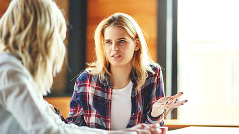 Two young female friends chatting over coffee in cafe. Blonde women discussing issues