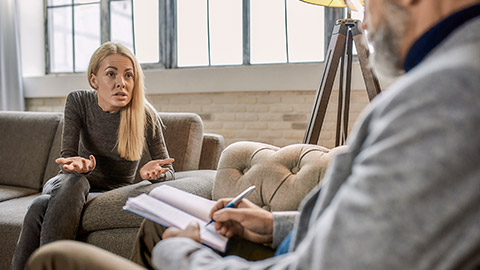 Angry young caucasian woman talking about her problems with psychotherapist during appointment in office, selective focus.