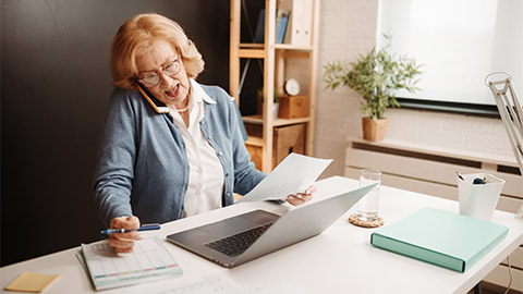 woman having a phone call while sitting in front of a laptop at the office.