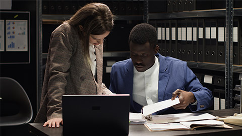 African american and caucasian inspectors collecting clues and information using, laptop and case files.