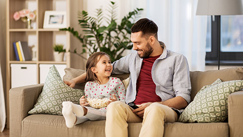 happy father and daughter with popcorn watching tv at home