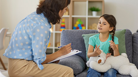 Supportive psychologist with clipboard listening to little child during therapy session