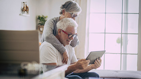 couple of seniors smiling and talking to their love ones with their gadget