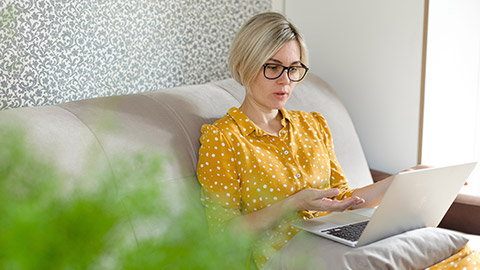 A woman sits on a couch with a laptop and talks via video link