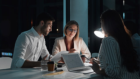 Teamwork, people and laptop in office at night with documents for deadline or overtime as accountant