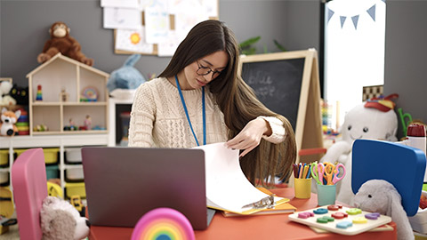 preschool teacher using laptop writing on document at kindergarten