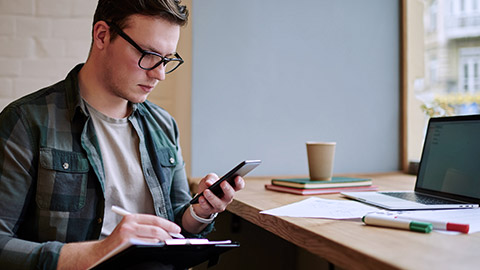 man writing with phone and laptop