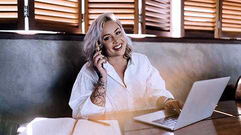 Creative woman smiling, working with computer while talking on the phone