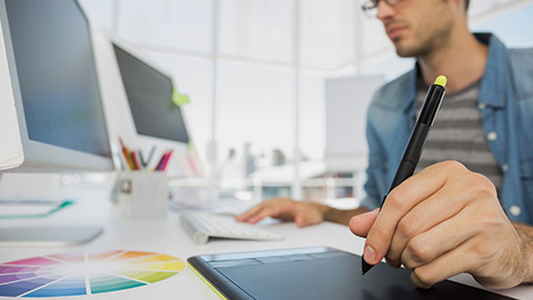 Side view of a casual male photo editor using graphics tablet in a bright office