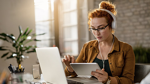 Young creative businesswoman working on digital tablet while wearing headphones in the office.