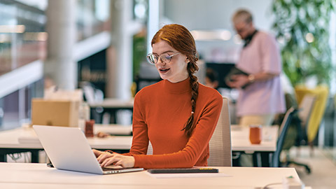 a professional businesswoman with orange hair sitting at her laptop