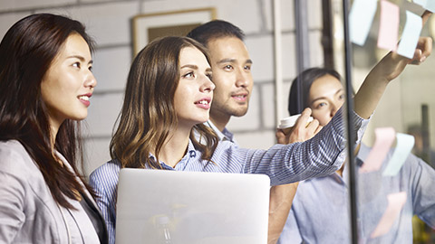 caucasian businesswoman pointing to a sticky note on glass wall during a brainstorming workshop in office