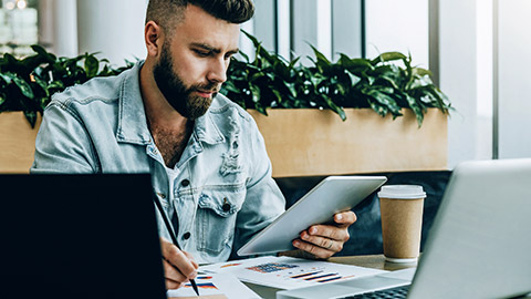 man is sitting in office in front of laptops, using digital tablet, making notes on chart