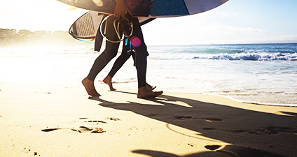 Two people walking on the beach holding surf boards and snorkling equipment