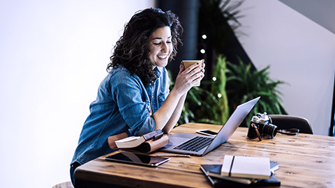 Smiling girl watching laptop, holding a cup