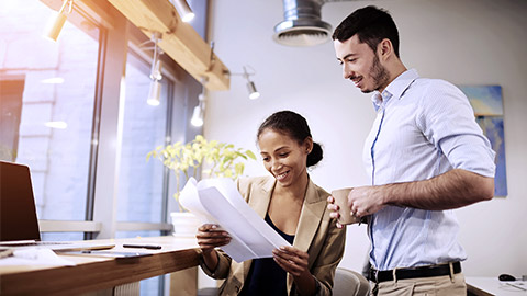 Female manager smiling while looking at co-worker's paper