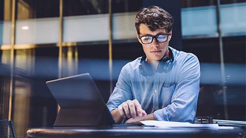 A person seated at a table in front of their tablet and some paperwork