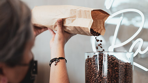 A close view of a barista refilling the coffee bean grinder