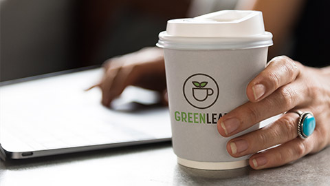 Close view of a person working on a laptop with a cup of GreenLeaf coffee in hand