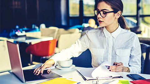 A busy project manager seated at a table, using scheduling tools available to them on their laptop