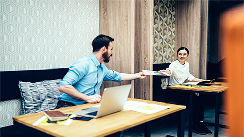 An employee handing finalised meeting minutes to a colleague for approval