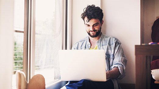 a man with a laptop happily working beside the window