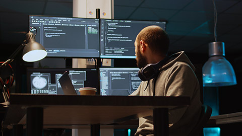 System programmer typing source code on laptop and multiple monitors