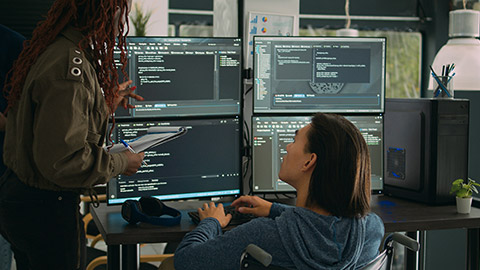 Female developer analyzing program code and talking to asian engineer