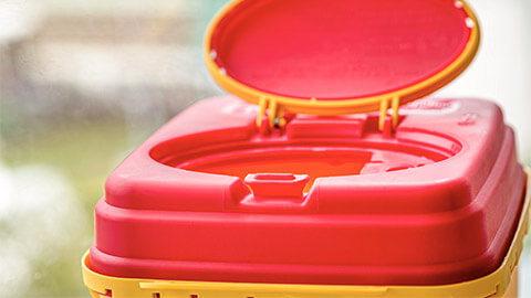 A close up of a sharps disposal unit with its lid open