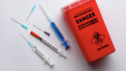 A shot of a sharps disposal unit, as well as different syringe components that go into it