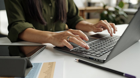 Hand of young female teacher or student typing on laptop keyboard while sitting by desk in front of camera and answering task questions