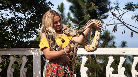 Happy woman tourist in yellow shirt holding snake python on shoulders and hands