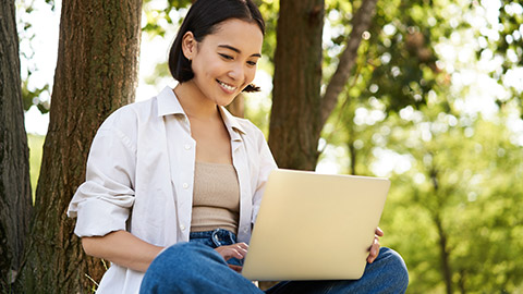 A person sitting outdoors working on a laptop