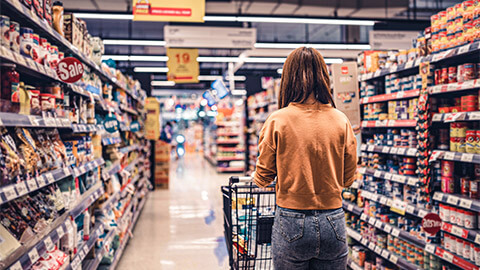 A person pushing a trolley down a well-lit, supermarket aisle, doing their weekly grocery shop