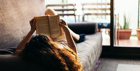 a person reading a book while lying on the couch