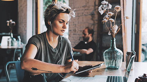 A designer sitting in a coffee shop with a laptop working on project scheduling