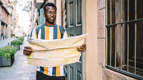 A young man referring to a map while walking down a quiet laneway, late in the afternoon