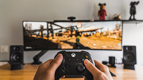 A close up of a person holding a wireless game console controller, seated in front of a large, curved screen