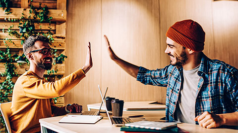 Two professionals in a common area at their workplace, high-fiving after reaching a project milestone