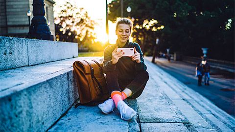 A student seated on a building's steps, watching a video on their smart phone