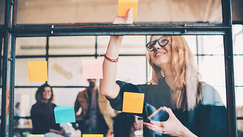 A marketing executive working on ideas on sticky notes on a glass wall